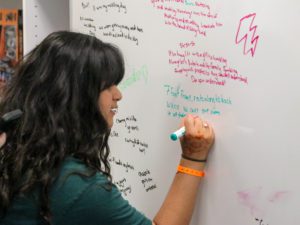 girl with dark hair writing on a white board | The ZONE